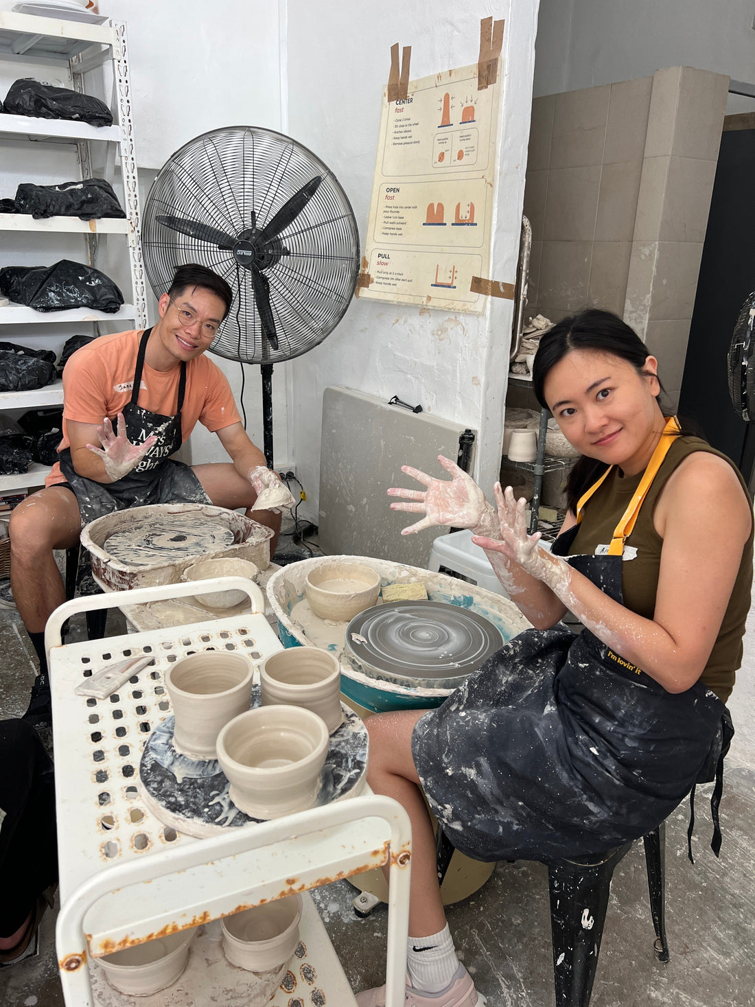 A couple sitting at wheels date night pottery wheel throwing class